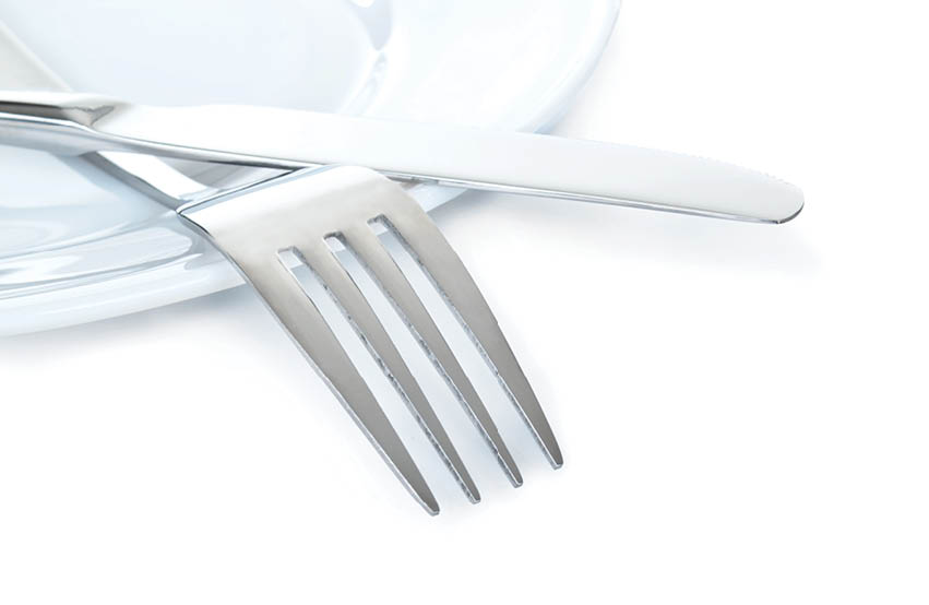 Close up of a silver knife and fork on plate isolated on white background